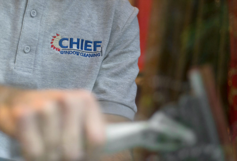 The Chief Window Cleaning logo on a team member's shirt, seen through clean glass
